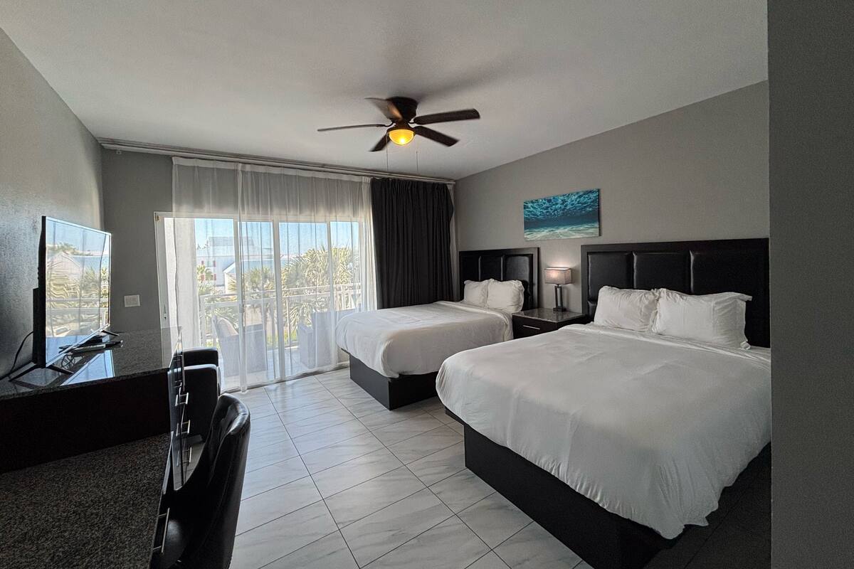 A hotel room with two beds, a ceiling fan, a TV, and a view of the outdoors.