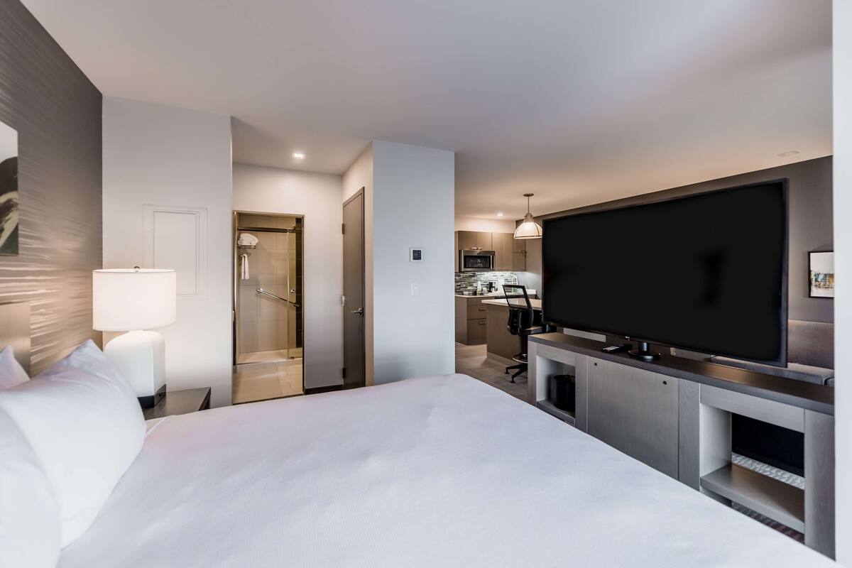A modern hotel room with a large bed, a TV, a desk, and a walk-in closet.