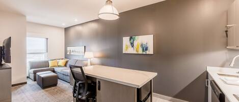A modern kitchen with a central island, a dining area with a sofa and a lamp, and a flat-screen TV.