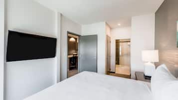 Habitació d'hotel moderna amb un llit gran, televisió de pantalla plana penjada a la paret, escriptori amb cadira i un bany visible a través d'una porta oberta.