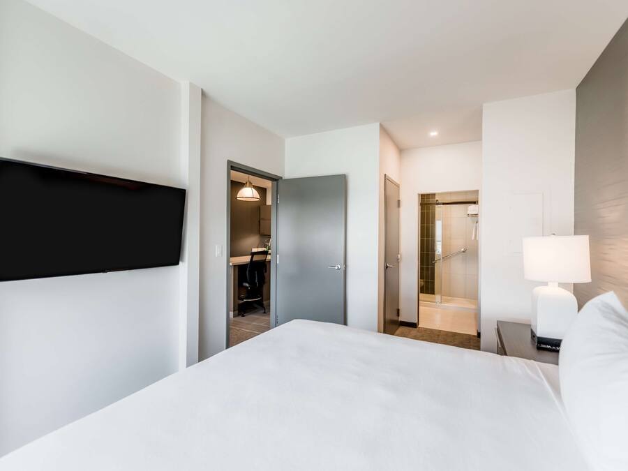 Habitació d'hotel moderna amb un llit gran, televisió de pantalla plana penjada a la paret, escriptori amb cadira i un bany visible a través d'una porta oberta.
