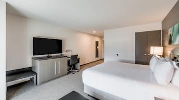 Habitación de hotel moderna con una cama grande, un escritorio con silla, un televisor y un armario.
