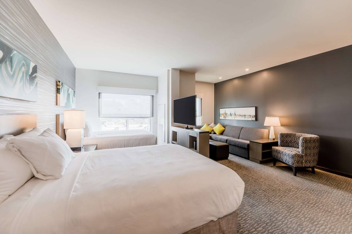 A modern hotel room with a large bed, a desk, a sofa, and a TV.