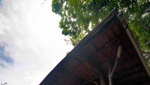 A wooden structure with a sloped roof supported by trees, featuring a deck with seating and a hammock. - Bahia Rica Fishing & Kayak Lodge (Paquera)