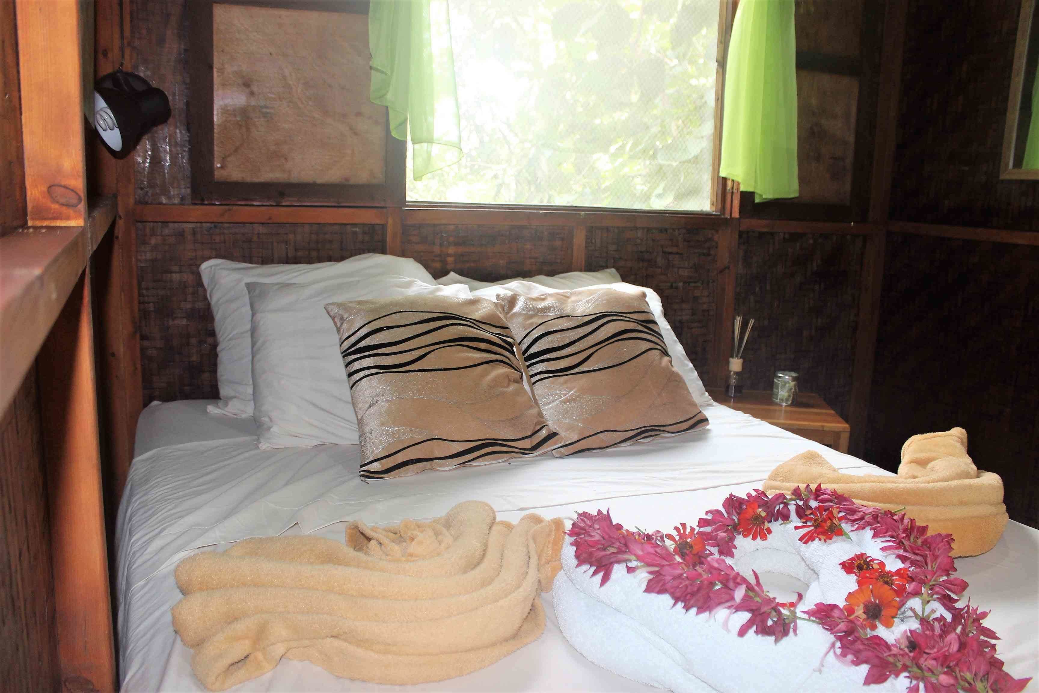 A neatly made bed with striped pillows, a towel, and a floral arrangement.