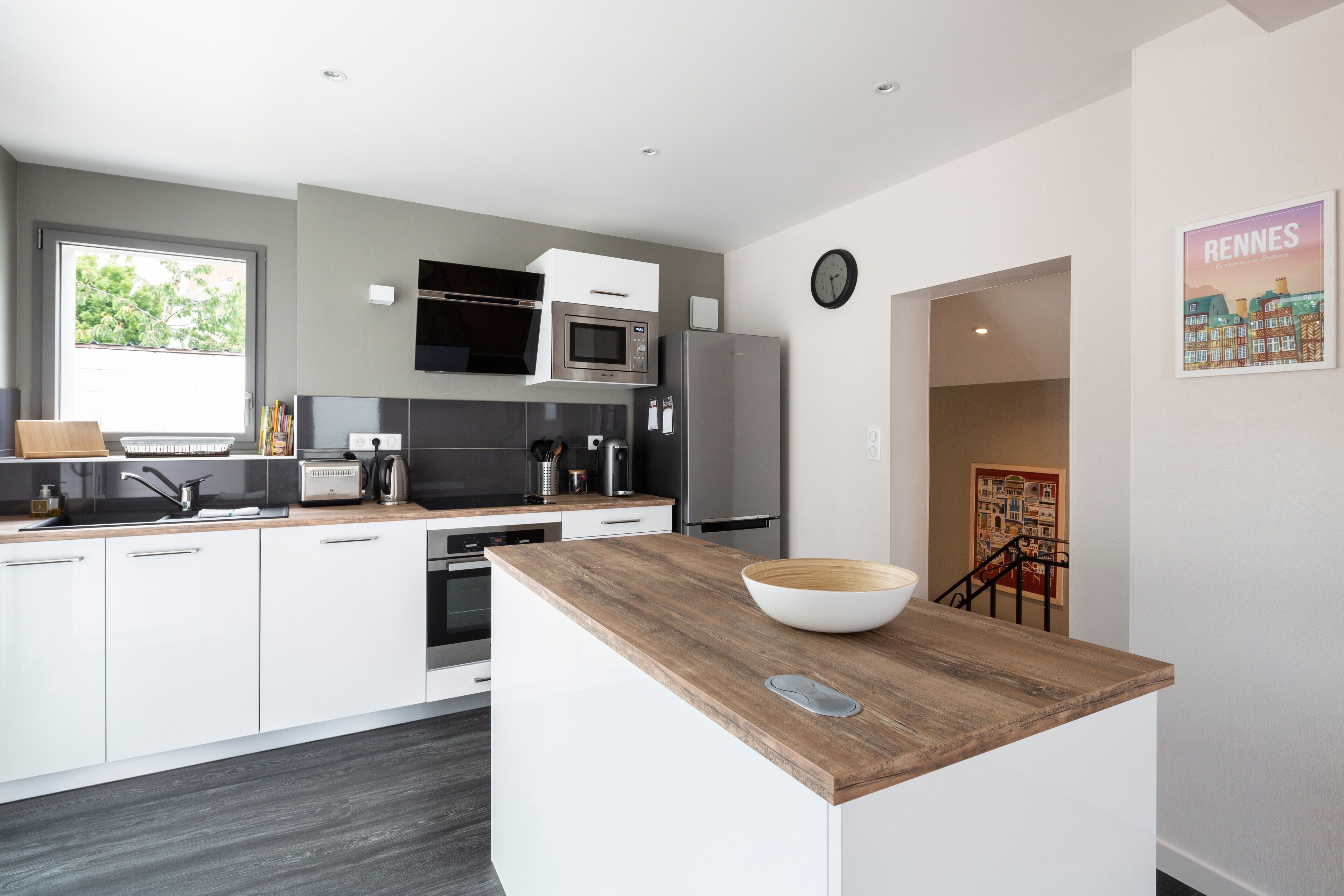 Een moderne keuken met witte kasten, een houten aanrecht, een magnetron, een koelkast en een spoelbak.