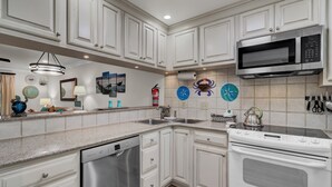 A modern kitchen with white cabinetry, stainless steel appliances, and decorative wall clocks. - 6C Mariners Walk | AvantStay | Easy Pool + Beach Access (Isle of Palms)
