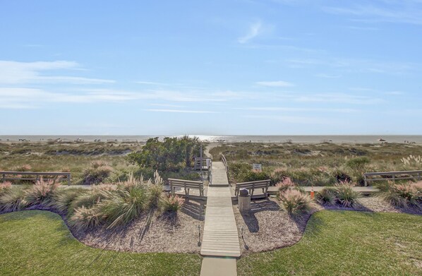 A wooden boardwalk leading to a beach area with dunes and sparse vegetation.