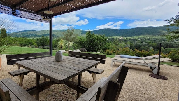 An outdoor patio with a wooden table and benches, surrounded by a gravel area and potted plants. - Villa in Dieulefit in Drome Provençale with views of nature and mountains (Dieulefit)