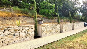 A stone retaining wall with a gravel path, a wooden bench, and a car parked on the side. - Villa in Dieulefit in Drome Provençale with views of nature and mountains (Dieulefit)