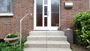 Un edificio in mattoni con una porta bianca, una cassetta delle lettere e un piccolo giardino con dei gradini che portano alla porta.