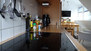 Una cucina moderna con piano cottura a induzione nero, zoccolo di piastrelle bianche e utensili in acciaio inossidabile appesi al muro.