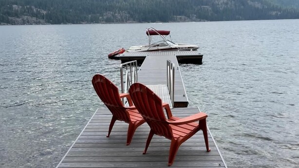 A wooden dock extending into a lake with three red Adirondack chairs and a small table at the end. - McCall Lakefront Cabin with Dock & Stunning Views (McCall)