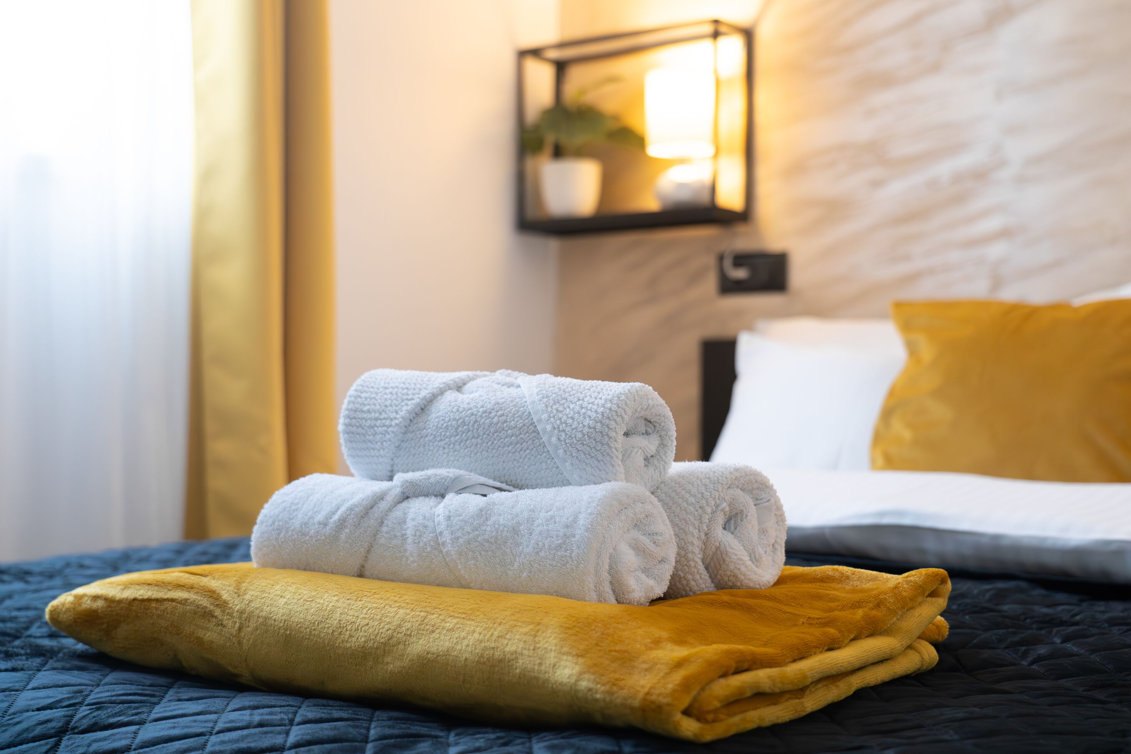 Un lit bien fait, avec des serviettes blanches et jaunes, une couvre-lit matelassée bleu foncé et un oreiller jaune.
