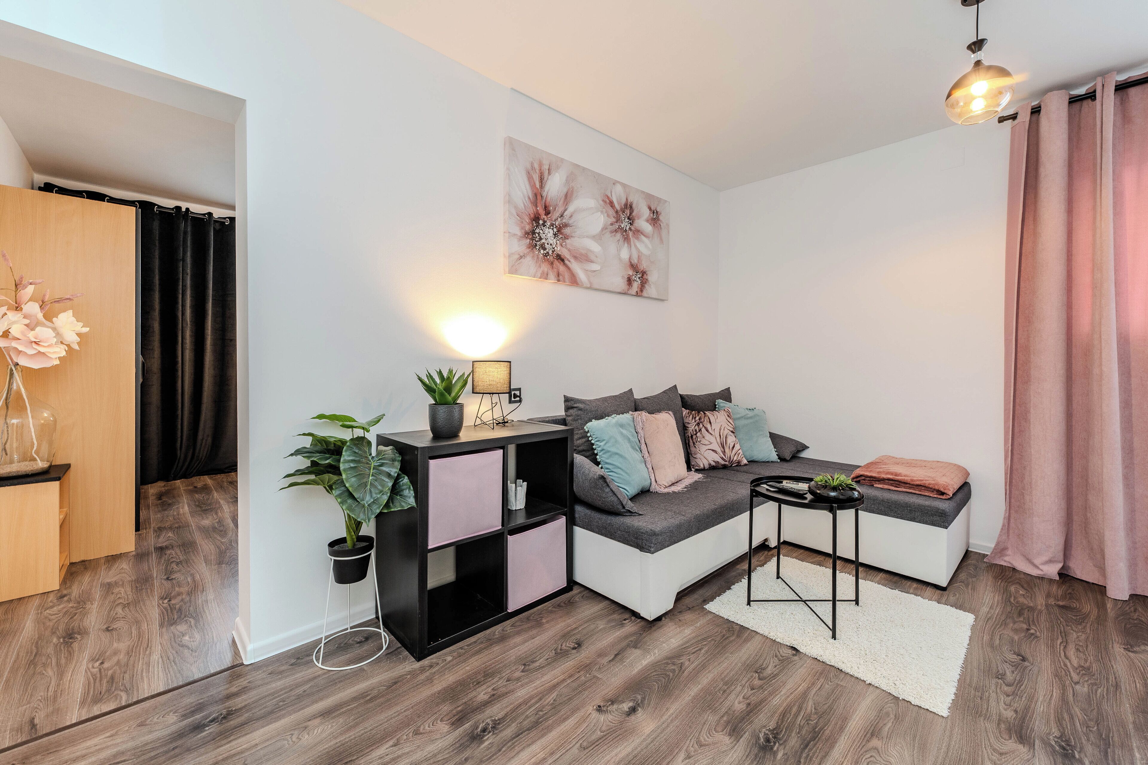 Un salon moderne avec un canapé d’angle, une table d’appoint, une plante en pot et une lampe fixée au mur.