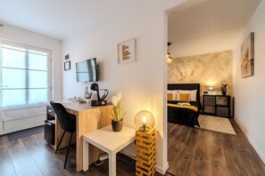 A modern apartment with a wooden desk, a small white table, a bed with a black headboard, and a large window. - Guesthouse Kod Spavalice (Vir)