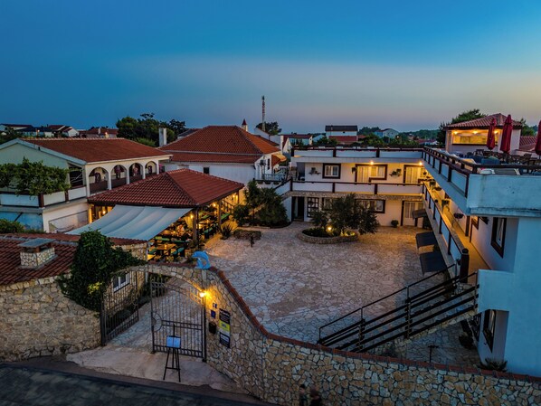 A courtyard with stone flooring, a covered seating area, and buildings with red-tiled roofs. - Guesthouse Kod Spavalice (Vir)