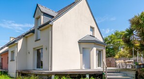 A two-story house with a flat roof, a balcony, and a patio area with outdoor furniture.