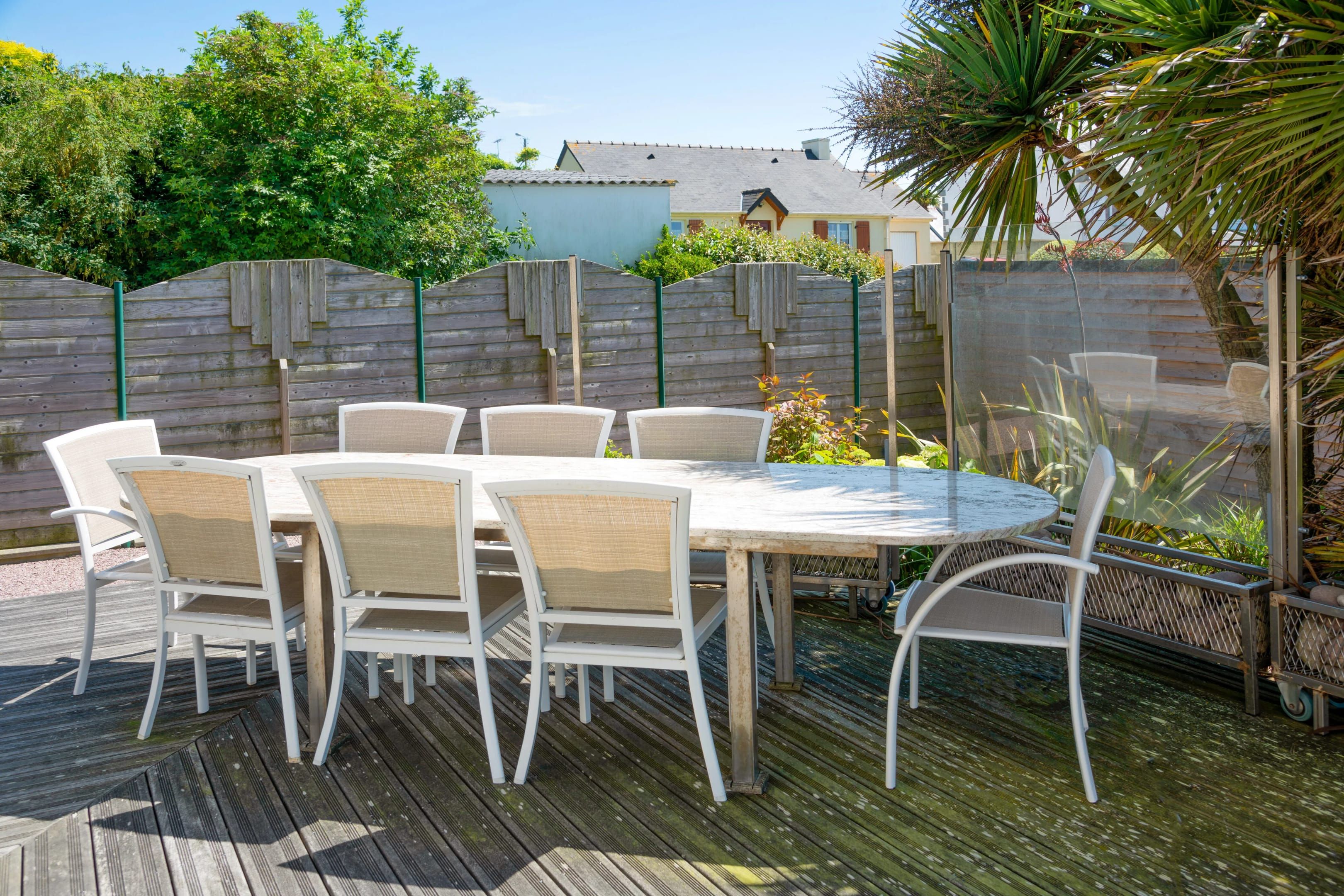 Une table ronde d’extérieur, entourée de chaises blanches, et le tout est installé sur une terrasse en bois.