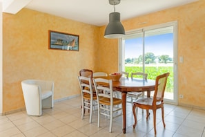Uma sala de jantar com mesa, cadeiras, um quadro e vista através de uma porta de vidro.