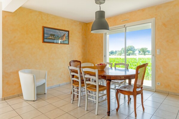 A dining area with a table, chairs, a painting, and a view through a glass door.