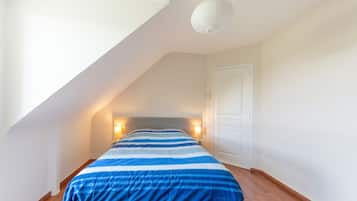 Ein Schlafzimmer mit geneigter Decke, einem Bett mit gestreifter Bettdecke, Nachttischlampen und einer weißen Tür.