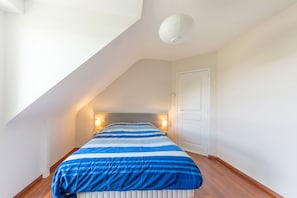 A bedroom with a sloped ceiling, a bed with a striped bedspread, bedside lamps, and a white door.