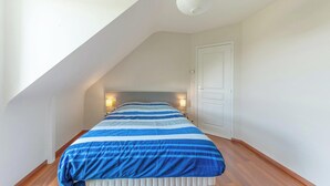 A bedroom with a sloped ceiling, a bed with a striped bedspread, two bedside lamps, and a white door. - Homerez - House in Plurien (Plurien)