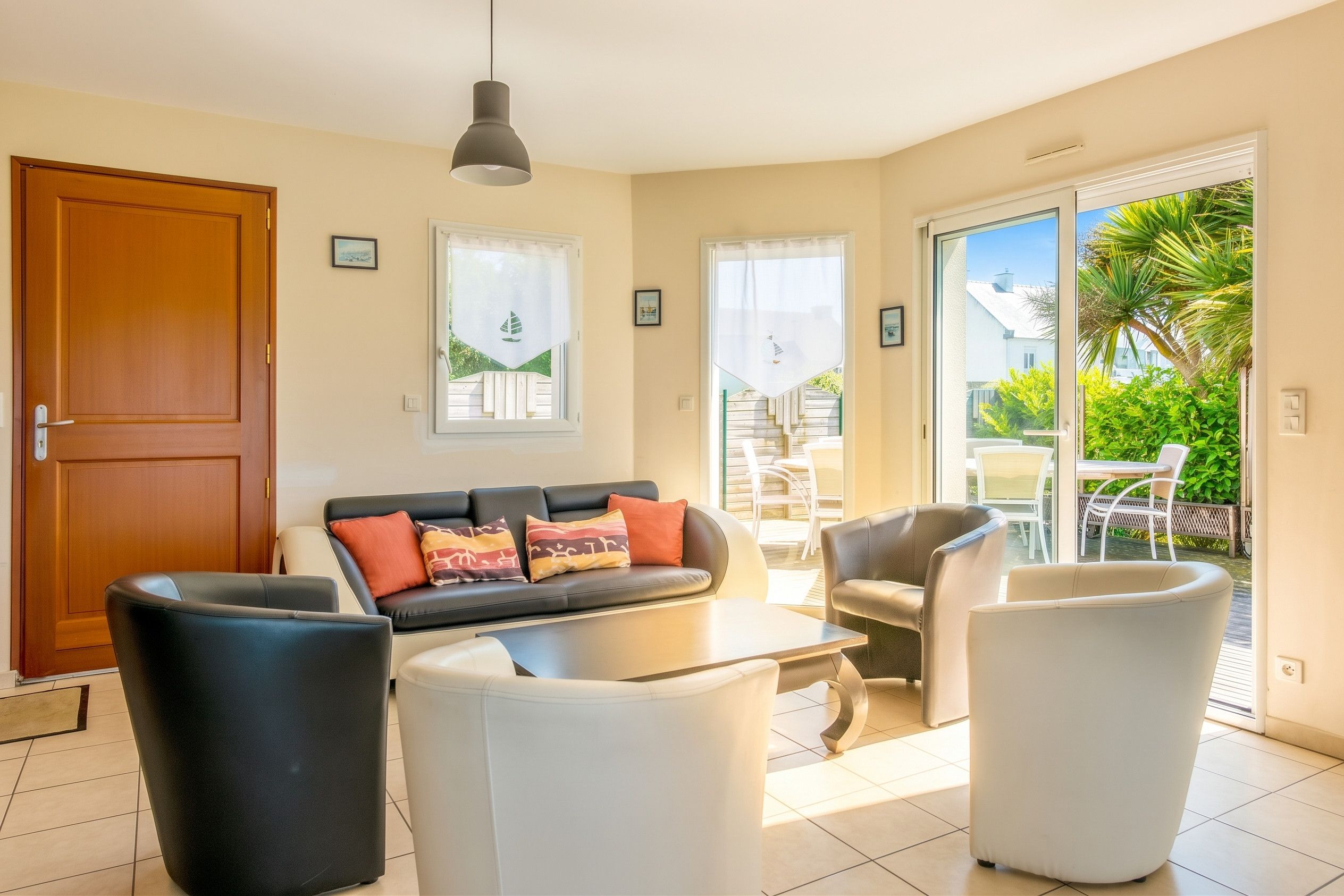 Un salon comprenant un canapé, deux fauteuils, une table basse et une porte-fenêtre coulissante donnant sur un espace extérieur avec une table et des chaises.