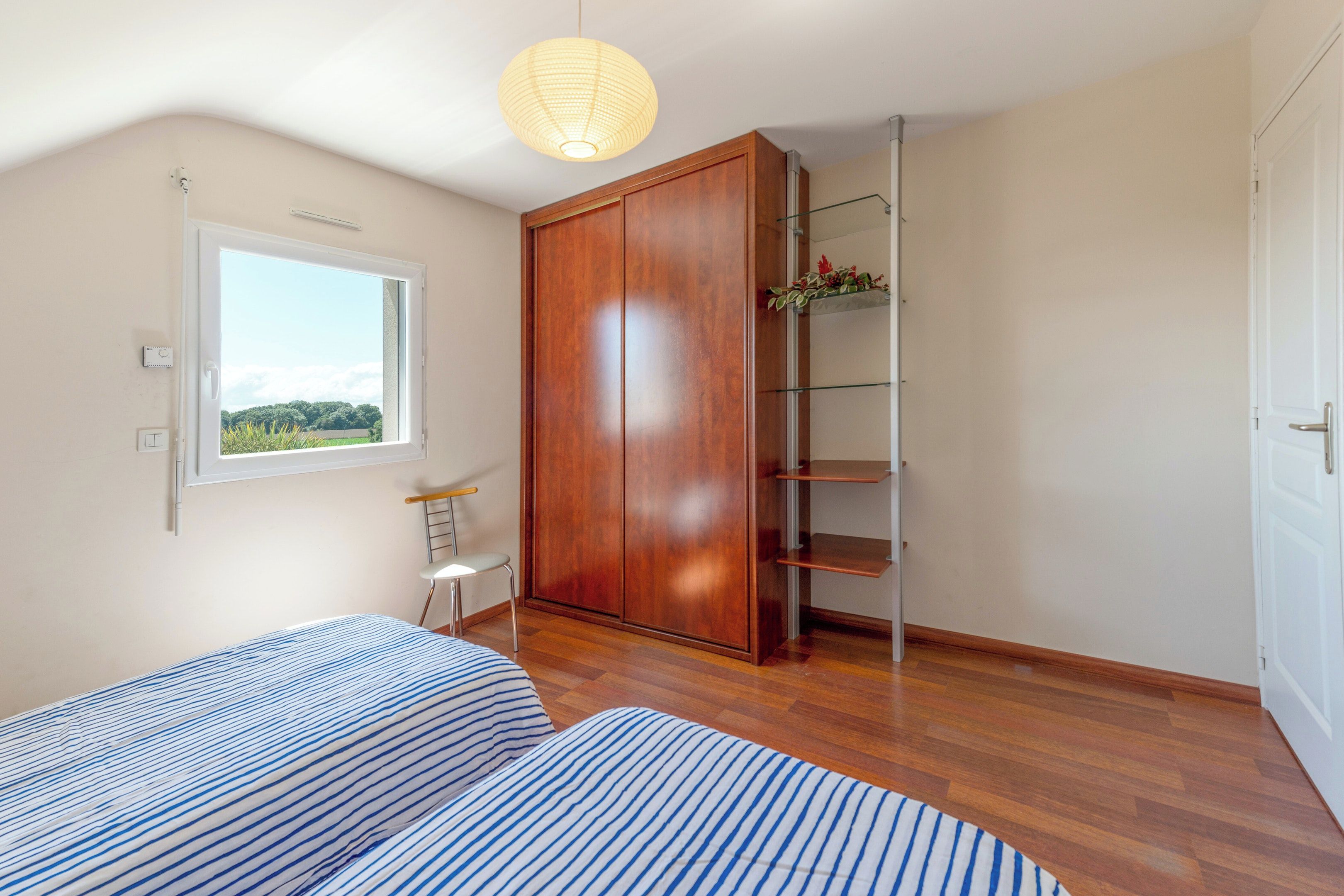 Ein Schlafzimmer mit Bett, Schrank, Fenster und einem Regal mit Pflanzen.