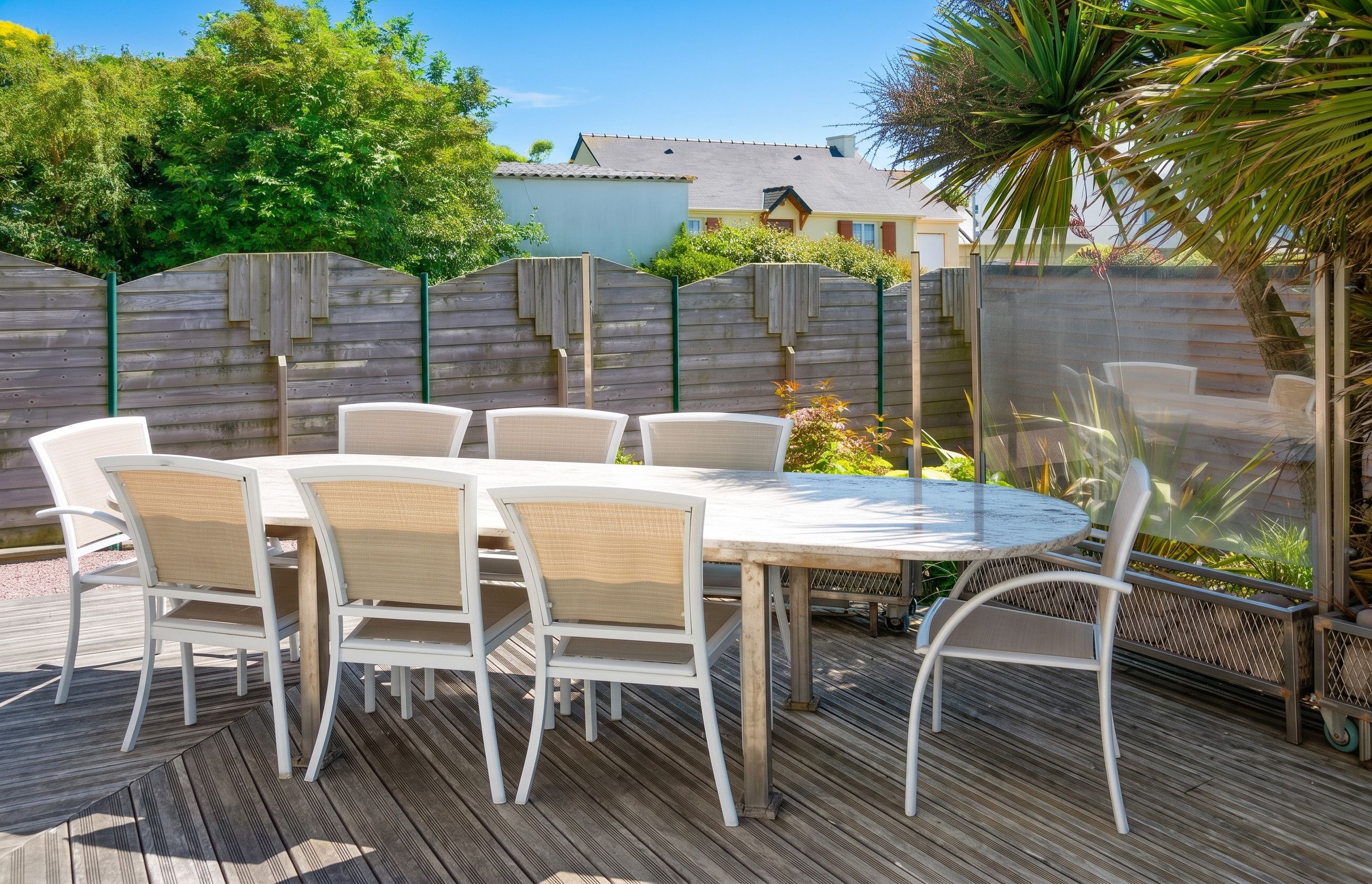 Une terrasse extérieure avec une table ronde et six chaises, entourée d’une plateforme en bois et d’une clôture en bois.