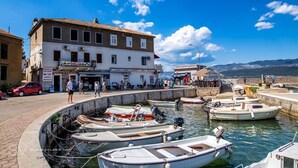 Uma área à beira-mar com barcos atracados, um edifício com placa de posto de turismo e montanhas ao fundo.