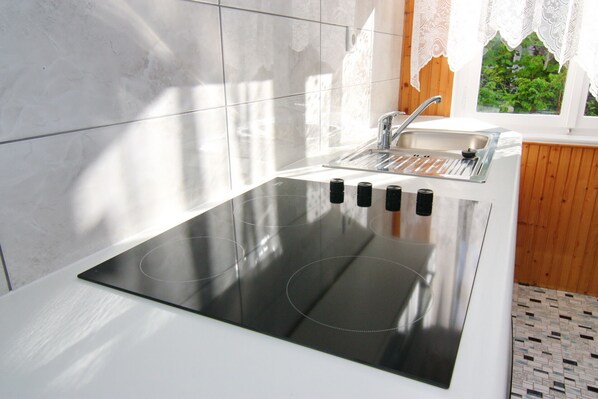 A modern kitchen with a built-in stovetop, a sink, and a window with lace curtains.