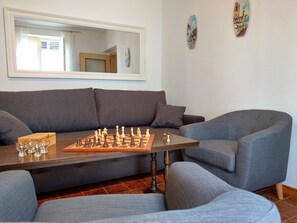 A living room with a chessboard on a wooden table, grey sofas, and a large mirror on the wall.