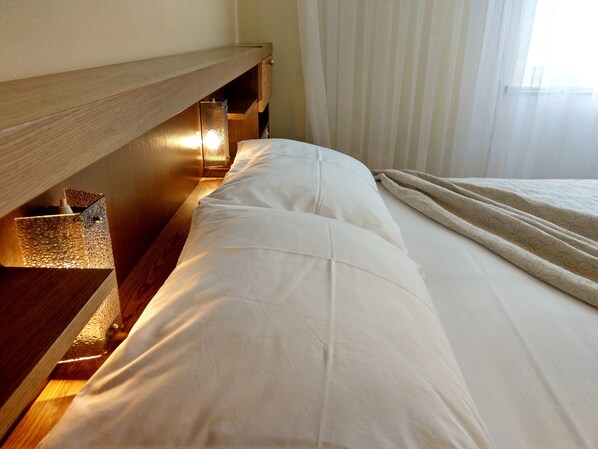 A neatly made bed with white linens, a wooden headboard, and a bedside table with a lamp.