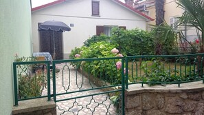 A house with a tiled patio, a green metal gate, and a number 112 sign.