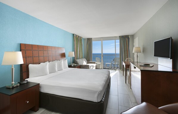 Habitación de hotel con una cama grande, un escritorio, una silla, un televisor y un balcón con vista al océano.