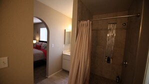 Une salle de bain moderne avec une douche, des toilettes et un lavabo. Un rideau est placé devant la douche, et un miroir est accroché au-dessus du lavabo.
