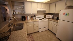 Une cuisine avec des meubles blancs, un évier en acier inoxydable, une cuisinière, un four à micro-ondes et un réfrigérateur.