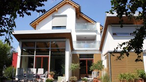 A modern two-story house with a balcony, outdoor seating area, and potted plants.