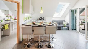 A modern kitchen with a dining area, featuring a central island with bar stools, a large window, and a skylight.
