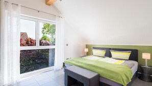 A bedroom with a bed, bench, and a view of trees through a window.
