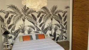 A bedroom with a bed, a white headboard, a wall with a tropical leaf pattern, a bedside table with a lamp, and a wooden floor. - 10-minute walk to the sea for 2 to 6 people (Le Relecq-Kerhuon)