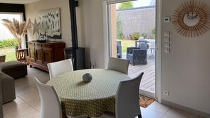 A dining area with a round table, white chairs, and a patterned tablecloth. There is a decorative wall piece and a large window with a view of the backyard. - 10-minute walk to the sea for 2 to 6 people (Le Relecq-Kerhuon)