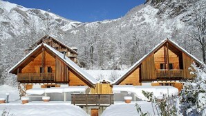 Zwei Holzhütten mit Balkonen vor einer verschneiten Berglandschaft.