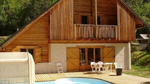 Eine Holzhütte mit Balkon, Pool und Gartenmöbeln.