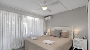 A neatly arranged bedroom with a bed, a nightstand, a ceiling fan, and a window with sheer curtains. - Spacious apartment in very well maintained complex.  Walk to beach. (Point Lookout)