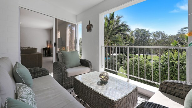 A balcony with wicker furniture, a glass door leading to an indoor area, and a view of greenery and a clear sky. - Spacious apartment in very well maintained complex.  Walk to beach. (Point Lookout)