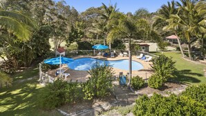 A swimming pool with lounge chairs and umbrellas, surrounded by palm trees and a fenced area. - Spacious apartment in very well maintained complex.  Walk to beach. (Point Lookout)