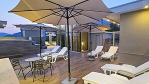 A rooftop terrace with sun loungers, a table, and umbrellas.